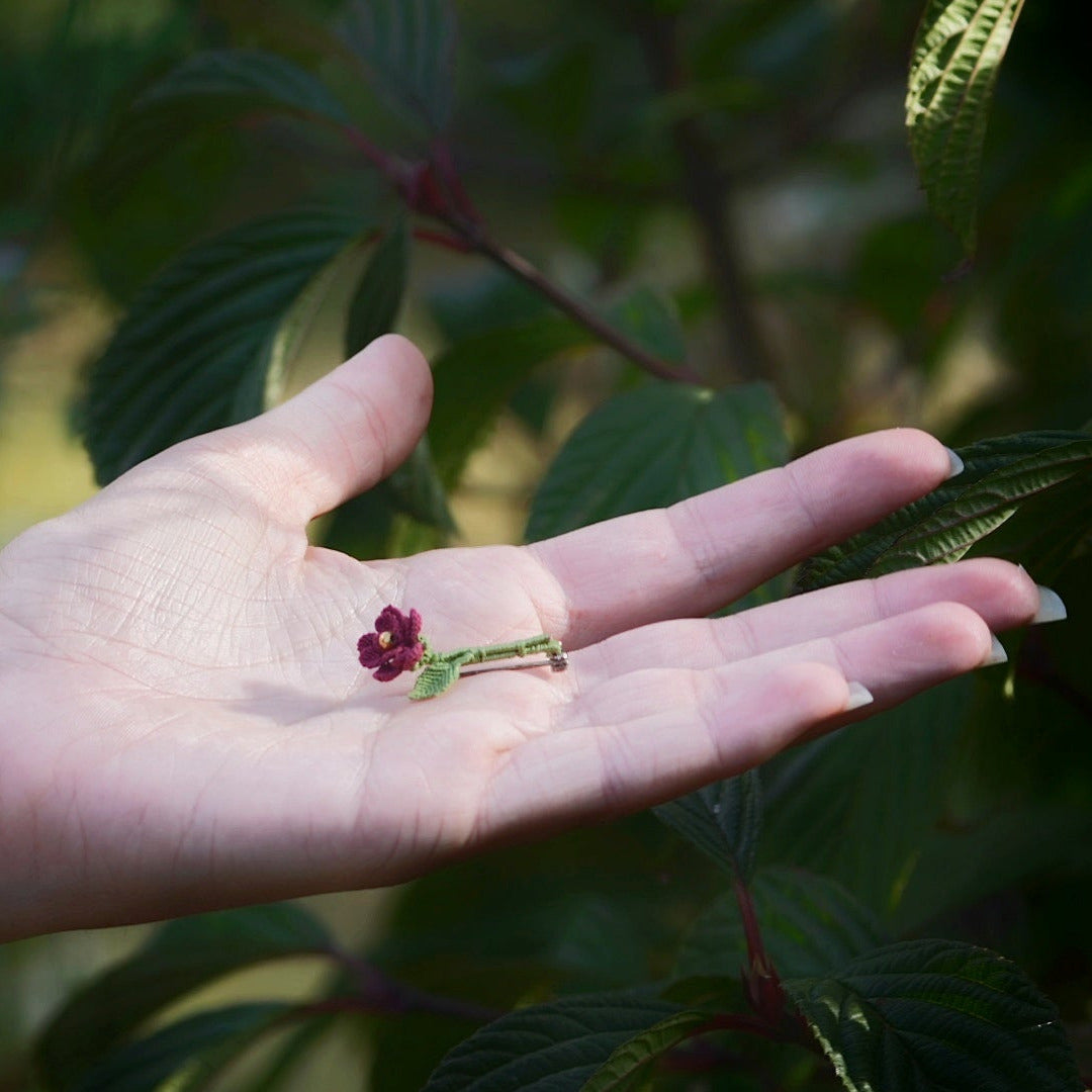 Broche artisanale fleur rouge en micro macramé, cœur doré, tenue à la main au milieu de feuilles vertes, bijou bohème elfique et fait main.