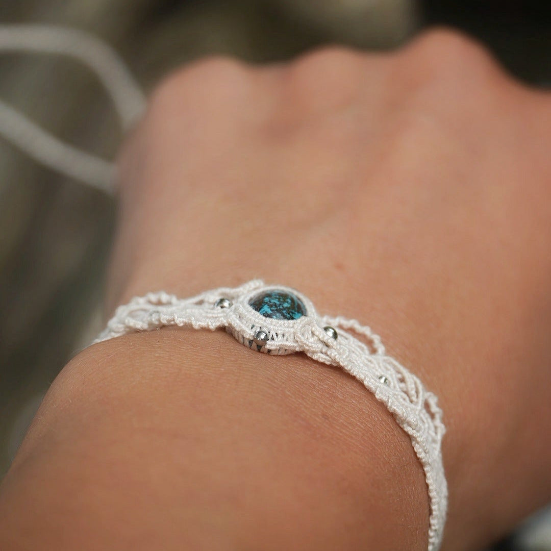 Bracelet large asymétrique. Bijou dentelle ambiance bohème hippie. Bracelet tissé en micro macramé avec fil de coton écru de 0.5 mm avec une pierre ovale de chrysocolle couleur bleu turquoise et marron foncé chocolat. Présence de part et d'autre de façon symétrique des perles en acier inoxydable argentées. Système de réglage à coulisse tubulaire à l'arrière. Design en relief et en torsade entrelacées celtiques. Ambiance plages, festival d'été, tribal. Bijou porté fond bois clair