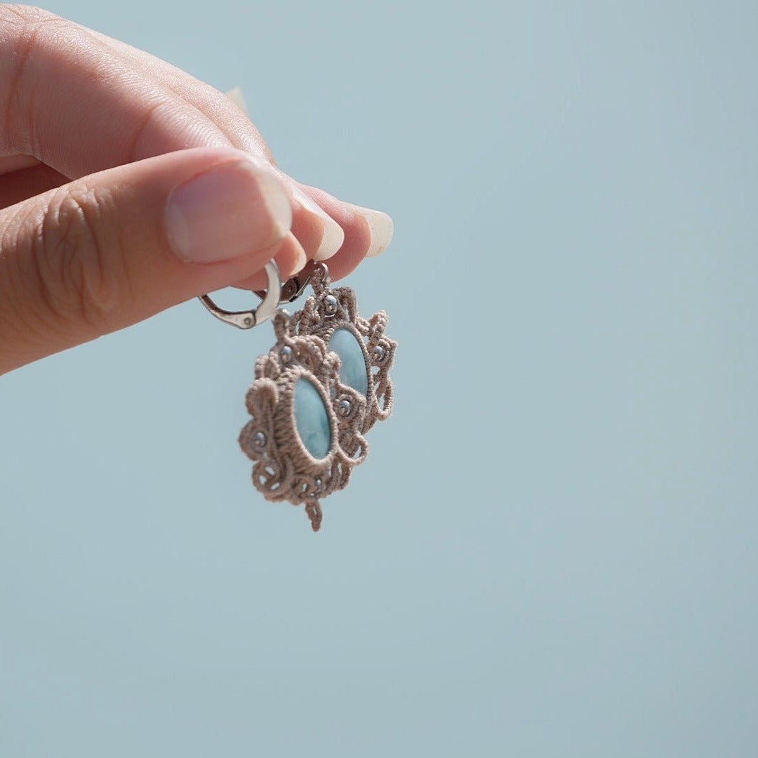 Boucles d'oreilles Trésors d'Ecume composée d'une Larimar bleu ciel ovales, mini Perles rondes en acier inoxydable argenté pour le côté luxe et précieux. Dormeuses en acier inoxydable pour un port assuré. Fil de Coton couleur lin naturel (beige gris) de 0, 5 mm tissé en micro-macramé en relief version celtique. Bijoux tenus en vertical avec fond bleu ciel marin et plage. Ambiance sirène, plage et tropiques, bohème et hippie. Parfait pour les tenues mariage et festivals.