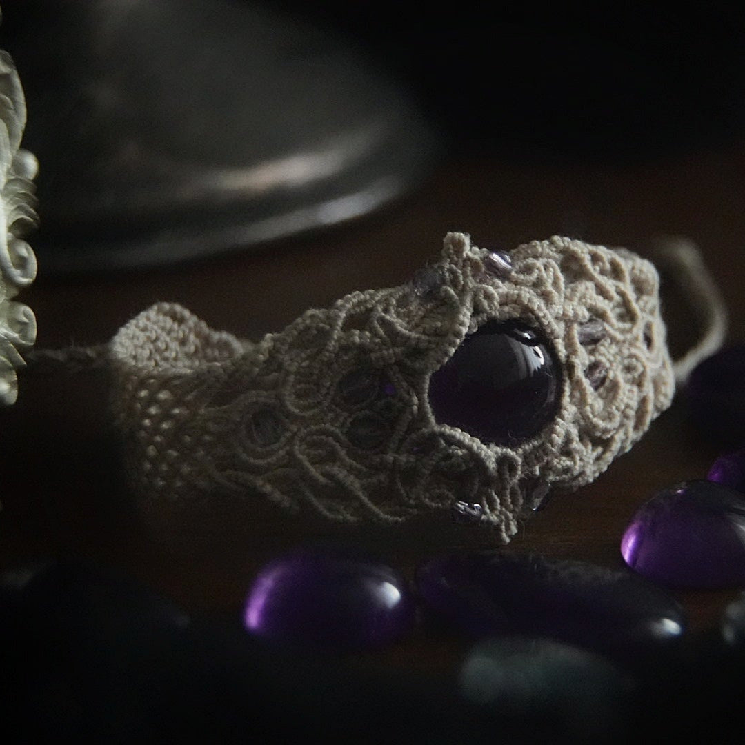 Bracelet large en macramé avec améthyste naturelle, bijou artisanal spirituel photographié dans un univers wicca gothique. Coton et Astrance