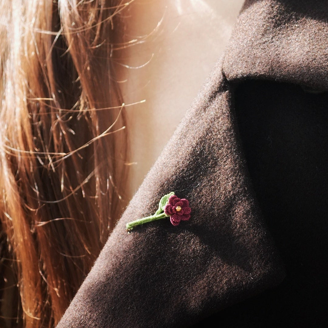 Broche florale rouge en micro macramé avec cœur doré, accessoire artisanal bohème et elfique, épinglée sur veste en laine marron foncé.