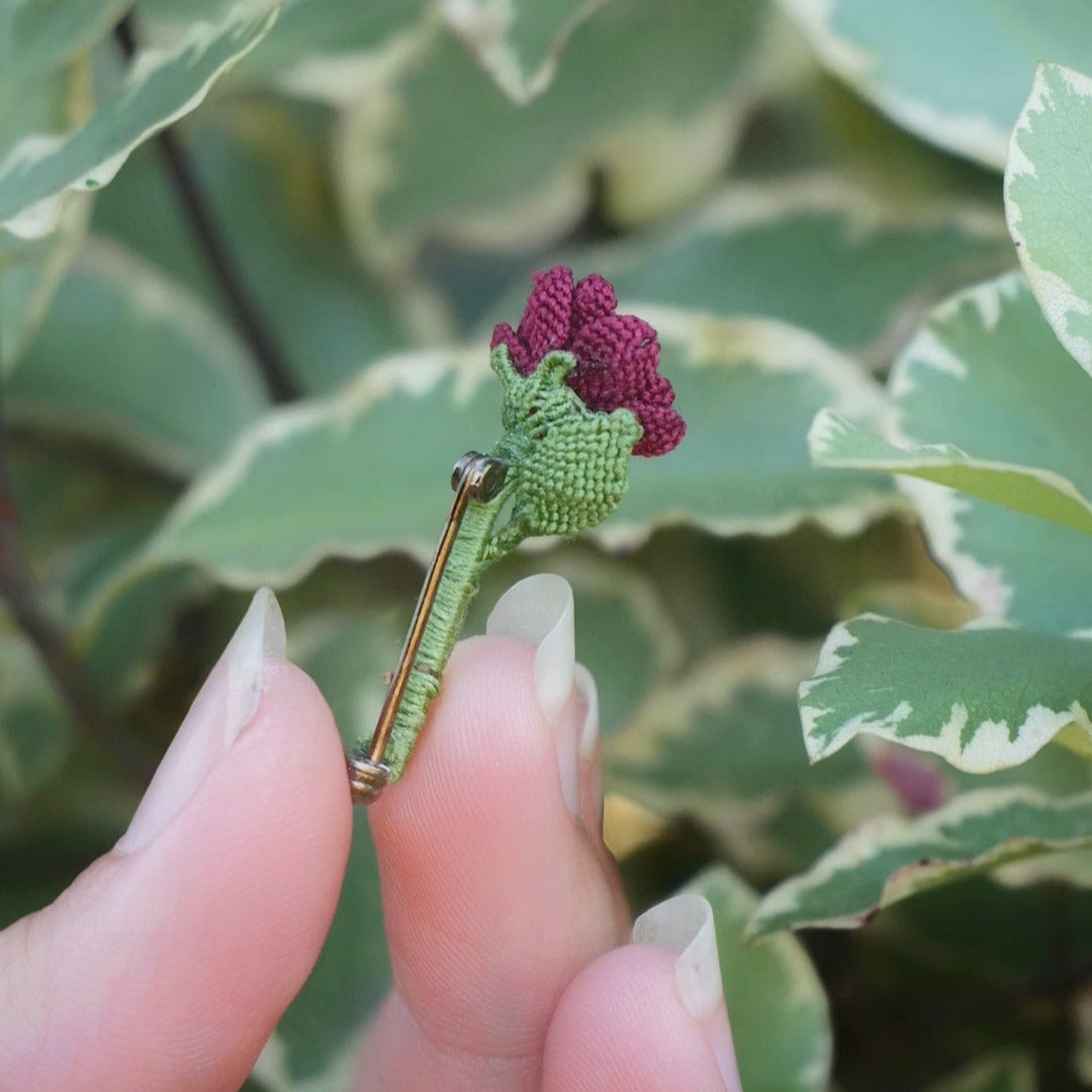Broche artisanale fleur rouge en micro macramé, cœur doré, tenue à la main au milieu de feuilles vertes, bijou bohème elfique et fait main.
