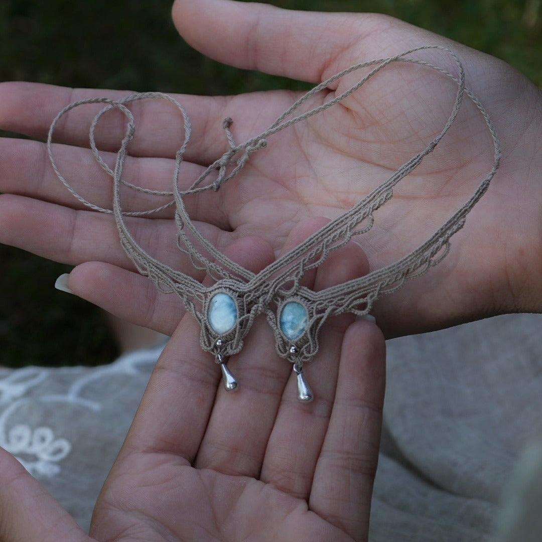 Duo de Bracelets de cheville bohème, ambiance plage et été sur les îles. Bijoux de pieds assortis. Micro macramé en fil de coton couleur lin beige avec une pierre de larimar bleu ciel accompagné d'une perle goutte argenté. Système de réglage à coulisse à l'arrière. Bijoux posé sur 2 mains dans un univers féérique bohème dans un jardin. Modèle avec Dreadlocks brunes, peau caramel et habits assorti au bijou de couleur lin naturel beige gris