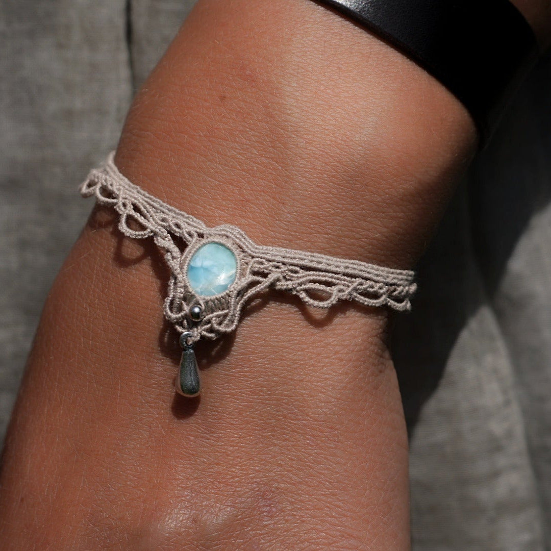 Duo de Bracelets bohème, ambiance plage et été sur les îles. Bijoux assortis. Micro macramé en fil de coton couleur lin beige avec une pierre de larimar bleu ciel accompagné d'une perle goutte argenté. Système de réglage à coulisse à l'arrière. Bijou porté sur une des poignets à la peau caramel dans un univers sirène, marin avec habits couleur lin beige gris assorti