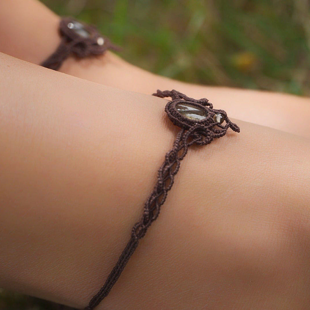 Bijoux de pieds, paire assortie de bracelets de chevilles à ambiance bohème celtique elfique. Fil marron foncé fin tissé en micro macramé avec entrelacs et arabesques, pierre centrale ovale petite taille jaune miel translucide. Bijoux hippie, bohème avec inspiration nature. Chevillères portées sur des chevilles à la peau pâle, bijoux pris de côté