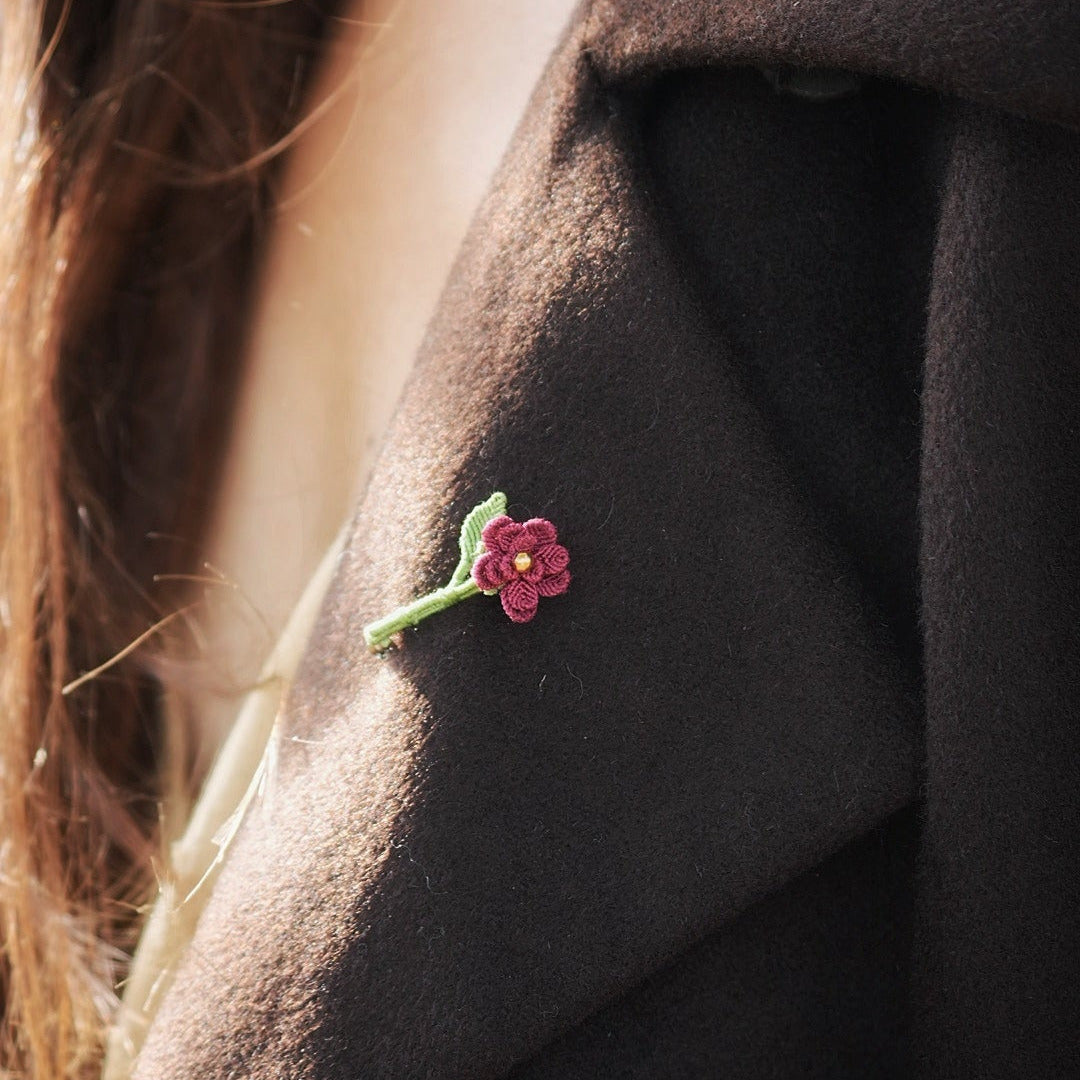 Broche florale rouge en micro macramé avec cœur doré, accessoire artisanal bohème et elfique, épinglée sur veste en laine marron foncé.