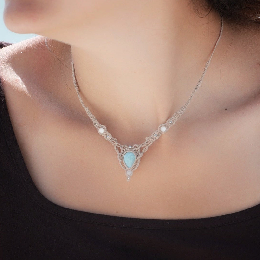 Collier ras-de-cou forme v Trésors d'Ecume composée d'une Larimar bleu ciel en poire pointe en bas, perles en nacre blanche ronde rappel des coquillages et de la plage, mini Perles rondes en acier inoxydable argenté pour le côté luxe et précieux. Fil de Coton couleur lin naturel (beige gris) de 0, 5 mm tissé en micro-macramé en relief version celtique. Collage 3 photos : Bijoux porté sur une femme bronzée et brune avec débardeur marron foncé. Photo ambiance tropiques et plages, style bohème hippie