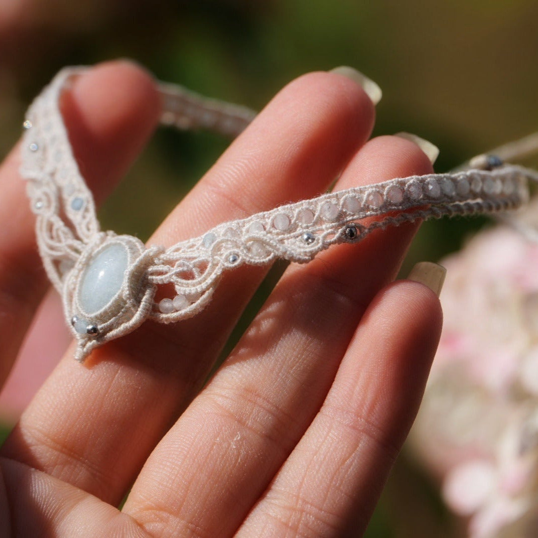 Bijou de cheville en micro macramé écru et aigue-marine posé sur une peau claire, bracelet mariage elfique et sirène. Coton et Astrance