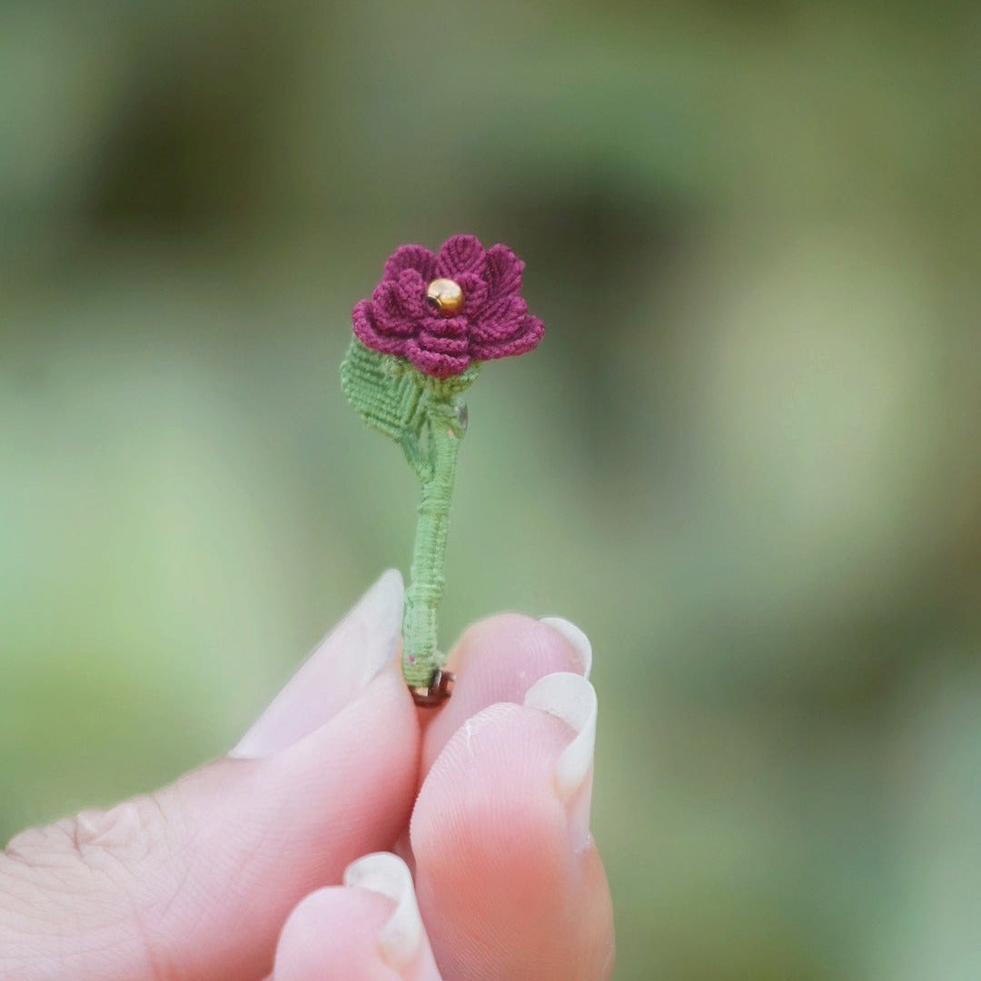 Broche artisanale fleur rouge en micro macramé, cœur doré, tenue à la main au milieu de feuilles vertes, bijou bohème elfique et fait main.