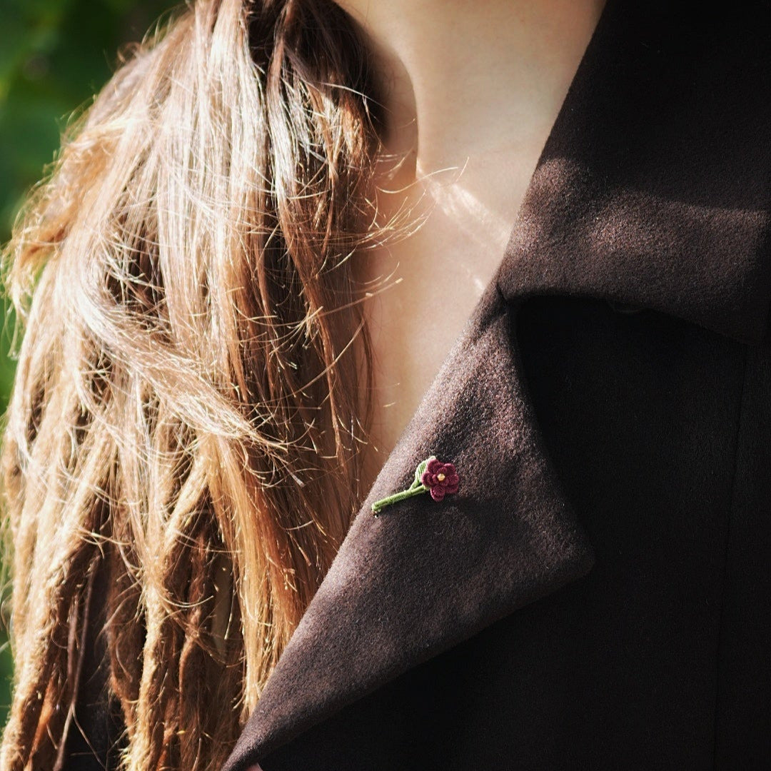 Broche florale rouge en micro macramé avec cœur doré, accessoire artisanal bohème et elfique, épinglée sur veste en laine marron foncé.