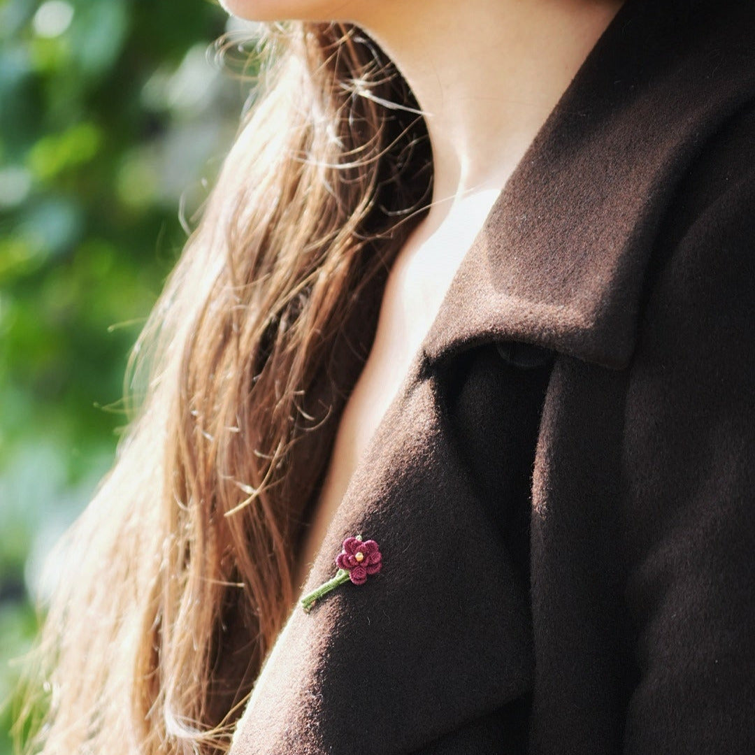 Broche florale rouge en micro macramé avec cœur doré, accessoire artisanal bohème et elfique, épinglée sur veste en laine marron foncé.