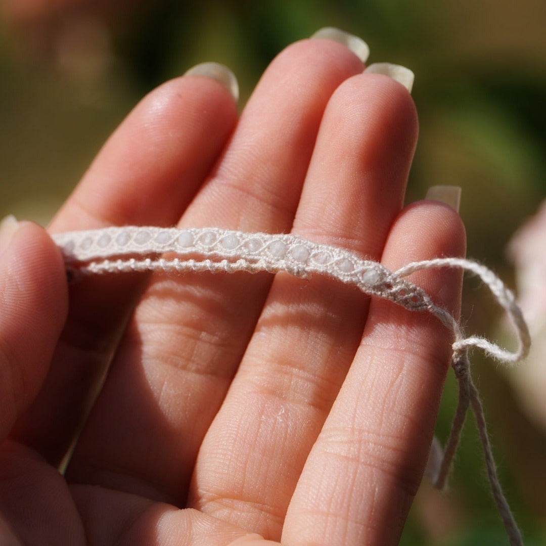 Bijou de cheville en micro macramé écru et aigue-marine posé sur une peau claire, bracelet mariage elfique et sirène. Coton et Astrance