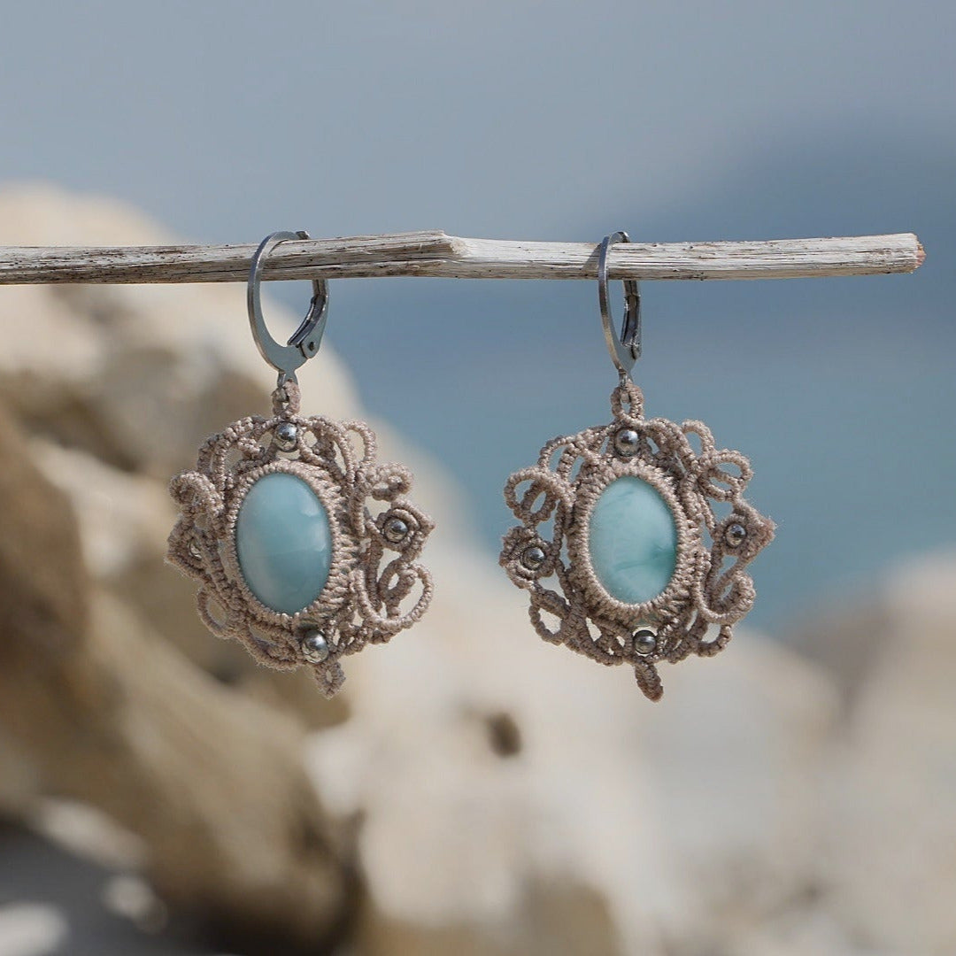 Boucles d'oreilles Trésors d'Ecume composée d'une Larimar bleu ciel ovales, mini Perles rondes en acier inoxydable argenté pour le côté luxe et précieux. Dormeuses en acier inoxydable pour un port assuré. Fil de Coton couleur lin naturel (beige gris) de 0, 5 mm tissé en micro-macramé en relief version celtique. Bijoux en vertical sur un bois flotté avec fond marin et plage, cailloux blanc et océan bleu. Ambiance sirène, plage et tropiques, bohème et hippie. Parfait pour les tenues mariage et festivals.