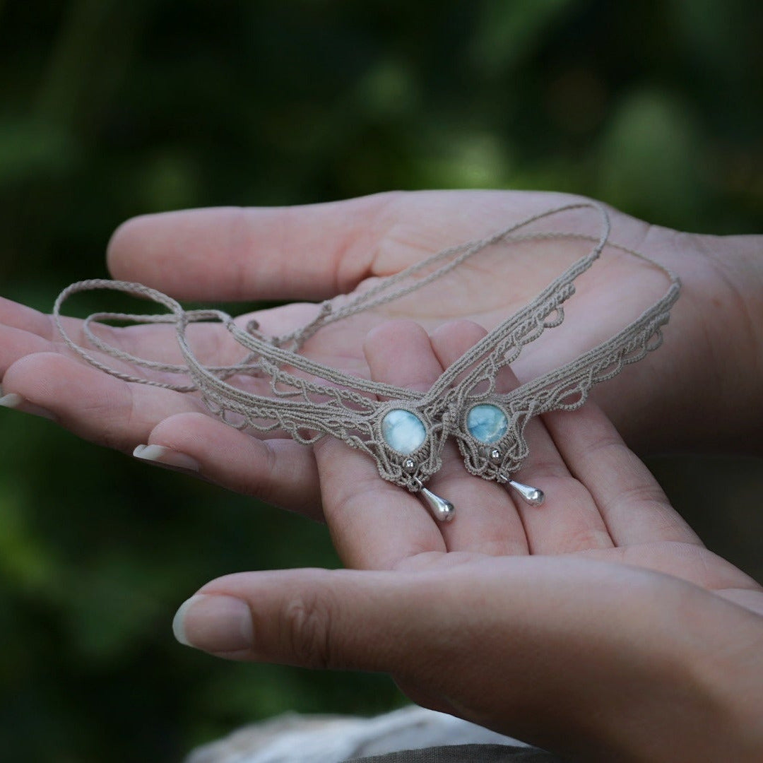 Duo de Bracelets de cheville bohème, ambiance plage et été sur les îles. Bijoux de pieds assortis. Micro macramé en fil de coton couleur lin beige avec une pierre de larimar bleu ciel accompagné d'une perle goutte argenté. Système de réglage à coulisse à l'arrière. Bijoux posé sur 2 mains dans un univers féérique bohème dans un jardin. Modèle avec Dreadlocks brunes, peau caramel et habits assorti au bijou de couleur lin naturel beige gris
