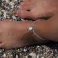 Duo de Bracelets de cheville bohème, ambiance plage et été sur les îles. Bijoux de pieds assortis. Micro macramé en fil de coton couleur lin beige avec une pierre de larimar bleu ciel accompagné d'une perle goutte argenté. Système de réglage à coulisse à l'arrière. Bijou porté sur une cheville dénudée à la peau caramel dans un univers sirène, marin avec plage de  coquillages