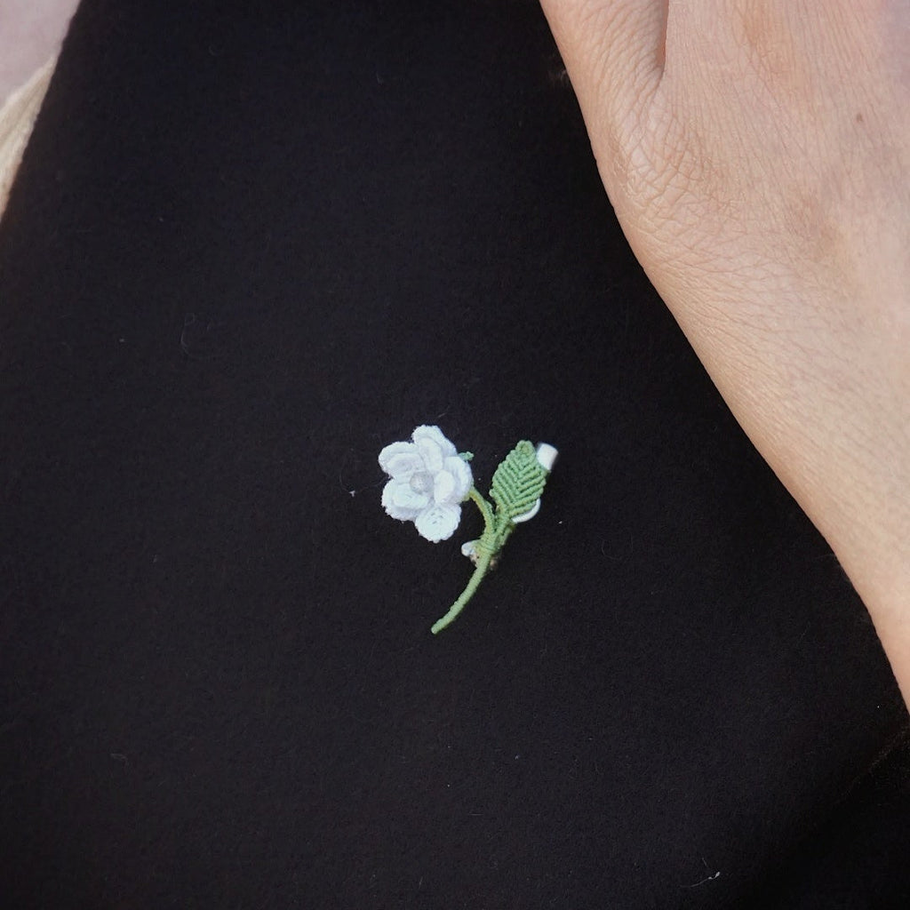 Mini broche fleur blanche en micro macramé avec cœur en labradorite bleu-vert, épinglée sur manteau en laine marron foncé, bijou elfique et bohème fait main.