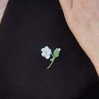 Mini broche fleur blanche en micro macramé avec cœur en labradorite bleu-vert, épinglée sur manteau en laine marron foncé, bijou elfique et bohème fait main.