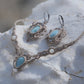 Parure Trésors d'Ecume composée d'une paire de boucles d'oreilles pendentes avec collier ras de cou assorti. Larimar bleu ciel ovales pour les boucles et en poire pointe en bas pour le collier. 3 Perles en nacre blanche pour le collier. Perles acier inoxydable argenté pour les deux pour le côté luxe et précieux. Dormeuses en acier inoxydable pour un port assuré. Fil de Coton couleur lin naturel (beige gris) de 0, 5 mm tissé en micro-macramé en relief version celtique. Bijoux posés sur une pierre blanche 