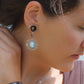Parure Trésors d'Ecume composée d'une paire de boucles d'oreilles pendentes avec collier ras de cou assorti. Larimar bleu ciel ovales pour les boucles et en poire pointe en bas pour le collier. 3 Perles en nacre blanche pour le collier. Perles acier inoxydable argenté pour les deux pour le côté luxe et précieux. Dormeuses en acier inoxydable pour un port assuré. Fil de Coton couleur lin naturel (beige gris) de 0, 5 mm tissé en micro-macramé en relief version celtique. Bijoux porté femme brune peau caramel