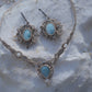 Parure Trésors d'Ecume composée d'une paire de boucles d'oreilles pendentes avec collier ras de cou assorti. Larimar bleu ciel ovales pour les boucles et en poire pointe en bas pour le collier. 3 Perles en nacre blanche pour le collier. Perles acier inoxydable argenté pour les deux pour le côté luxe et précieux. Dormeuses en acier inoxydable pour un port assuré. Fil de Coton couleur lin naturel (beige gris) de 0, 5 mm tissé en micro-macramé en relief version celtique. Bijoux posés sur une pierre blanche 