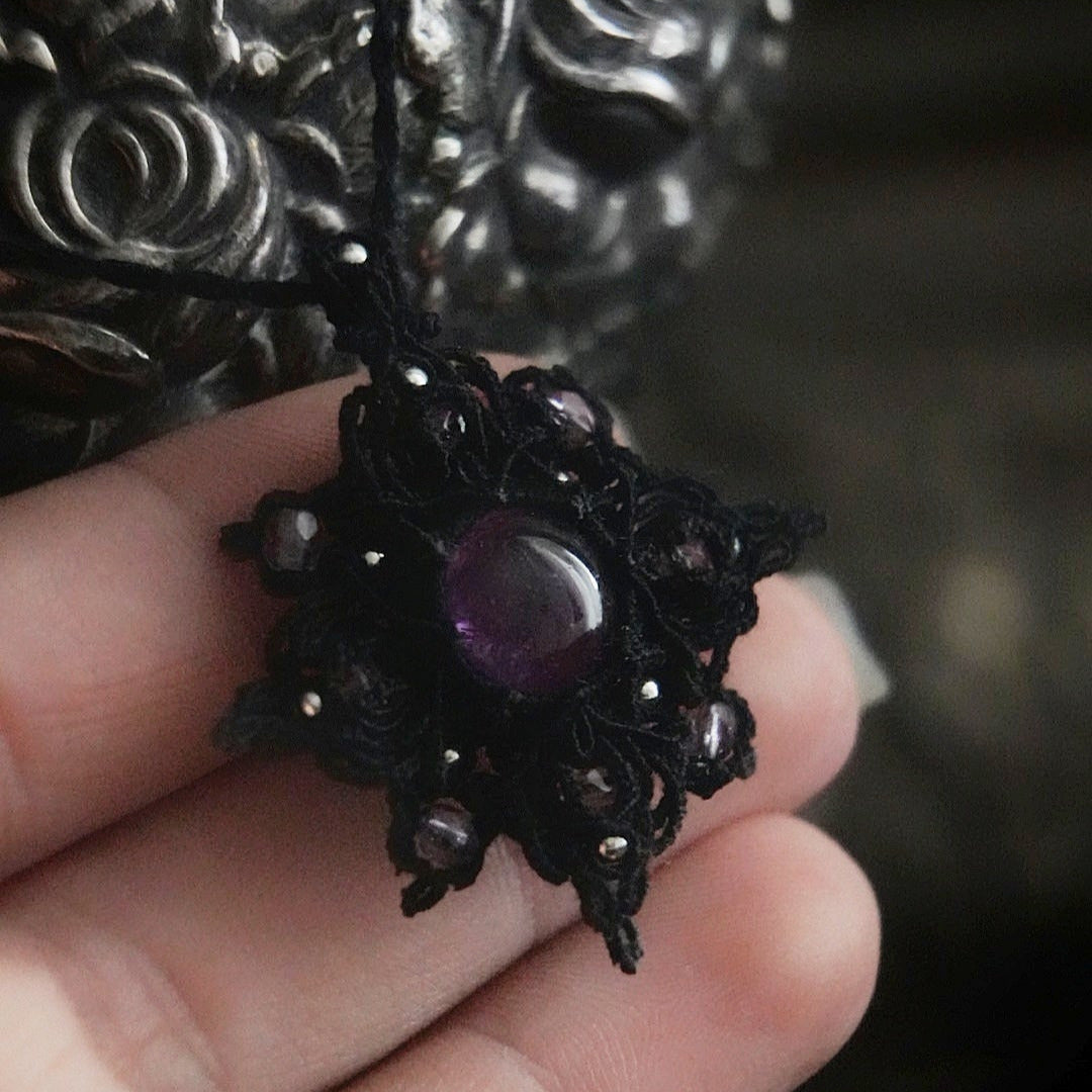 Bijou elfique sombre en micro macramé noir, pendentif étoile lumineux photographié sur fond gothique romantique. Coton et Astrance