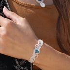Bracelet large asymétrique. Bijou dentelle ambiance bohème hippie. Bracelet tissé en micro macramé avec fil de coton écru de 0.5 mm avec une pierre ovale de chrysocolle couleur bleu turquoise et marron foncé chocolat. Présence de part et d'autre de façon symétrique des perles en acier inoxydable argentées. Système de réglage à coulisse tubulaire à l'arrière. Design en relief et en torsade entrelacées celtiques. Ambiance plages, festival d'été, tribal. Bijou porté sur tenue bohème baroudeur