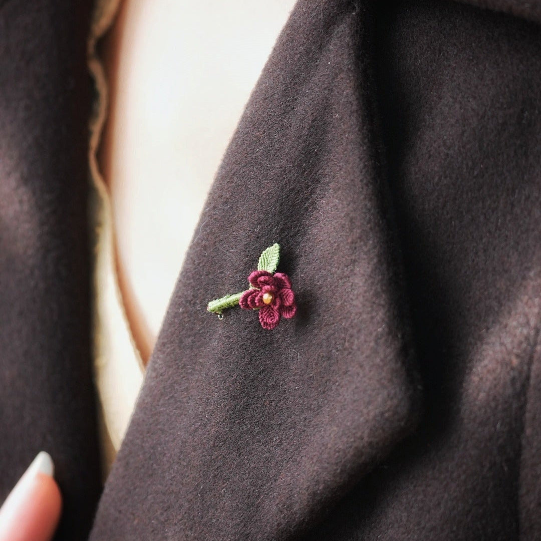 Broche florale rouge en micro macramé avec cœur doré, accessoire artisanal bohème et elfique, épinglée sur veste en laine marron foncé.