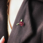 Broche florale rouge en micro macramé avec cœur doré, accessoire artisanal bohème et elfique, épinglée sur veste en laine marron foncé.