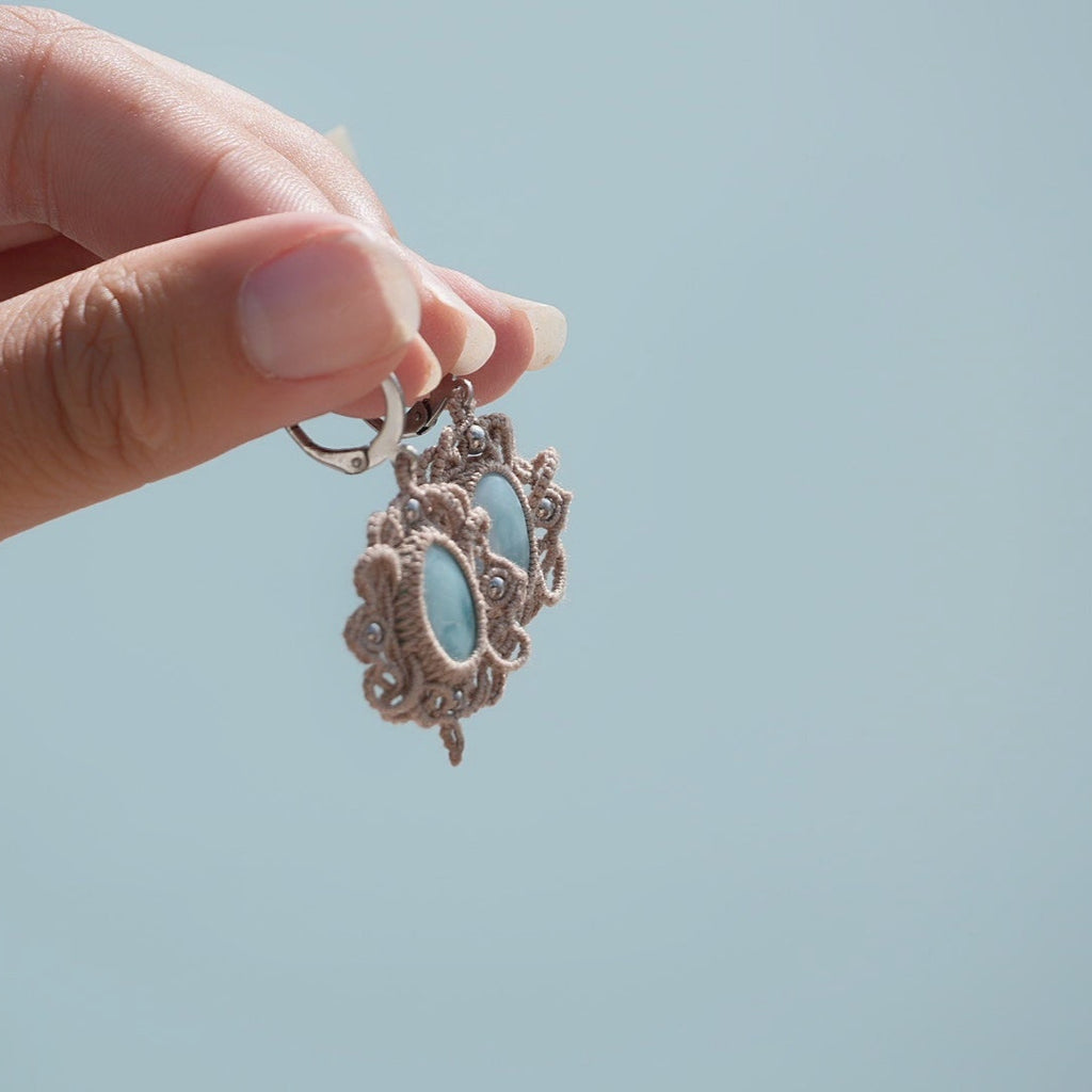 Boucles d'oreilles Trésors d'Ecume composée d'une Larimar bleu ciel ovales, mini Perles rondes en acier inoxydable argenté pour le côté luxe et précieux. Dormeuses en acier inoxydable pour un port assuré. Fil de Coton couleur lin naturel (beige gris) de 0, 5 mm tissé en micro-macramé en relief version celtique. Bijoux tenus en vertical avec fond bleu ciel marin et plage. Ambiance sirène, plage et tropiques, bohème et hippie. Parfait pour les tenues mariage et festivals. 