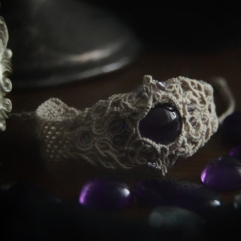 Bracelet large en macramé avec améthyste naturelle, bijou artisanal spirituel photographié dans un univers wicca gothique. Coton et Astrance