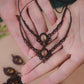 Bijoux de pieds, paire assortie de bracelets de chevilles à ambiance bohème celtique elfique. Fil marron foncé fin tissé en micro macramé avec entrelacs et arabesques, pierre centrale ovale petite taille jaune miel translucide. Bijoux hippie, bohème avec inspiration nature. Chevillères posées à plat dans 2 mains en coupe à la peau pâle, un bijou au dessus de l'autre avec en fond d'autres bijoux marron et jaune miel.