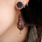 Boucles d'oreilles de style celtique elfique. Bijou féminin composé de : un tissage en relief avec arabesques en micro macramé avec du fil de coton marron foncé chocolat, pierre naturelle de citrine de forme goutte couleur jaune miel accompagné d'une perle ronde en citrine de 3 mm, d'un crochet doré en acier et d'une micro goutte bronze. Le bijou est porté sur une peau dorée et avec un fond de cheveux brun foncé, une main dans le cou avec une écharper aux tons orangers
