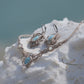 Parure Trésors d'Ecume composée d'une paire de boucles d'oreilles pendentes avec collier ras de cou assorti. Larimar bleu ciel ovales pour les boucles et en poire pointe en bas pour le collier. 3 Perles en nacre blanche pour le collier. Perles acier inoxydable argenté pour les deux pour le côté luxe et précieux. Dormeuses en acier inoxydable pour un port assuré. Fil de Coton couleur lin naturel (beige gris) de 0, 5 mm tissé en micro-macramé en relief version celtique. Bijoux posés sur une pierre blanche