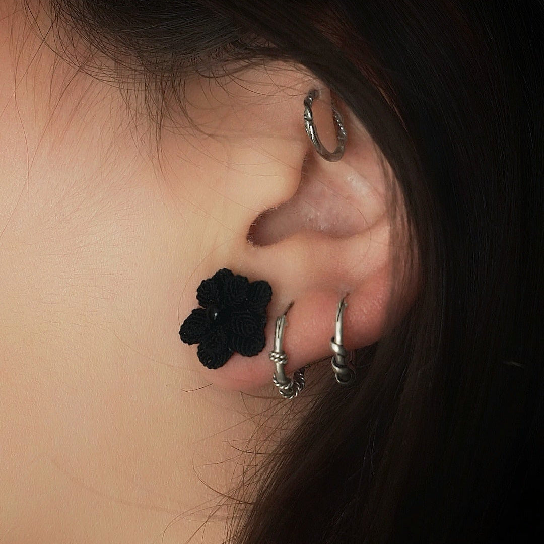 Boucles d’oreilles florales noires en onyx portées sur oreille féminine, bijou gothique artisanal en micro macramé. Coton et Astrance