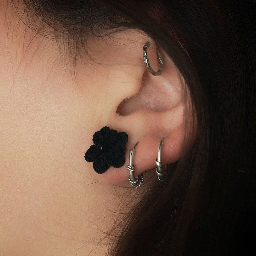 Boucles d’oreilles florales noires en onyx portées sur oreille féminine, bijou gothique artisanal en micro macramé. Coton et Astrance