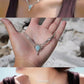 Collier ras-de-cou forme v Trésors d'Ecume composée d'une Larimar bleu ciel en poire pointe en bas, perles en nacre blanche ronde rappel des coquillages et de la plage, mini Perles rondes en acier inoxydable argenté pour le côté luxe et précieux. Fil de Coton couleur lin naturel (beige gris) de 0, 5 mm tissé en micro-macramé en relief version celtique. Collage 3 photos : Bijoux posés et porté sur une femme bronzée et brune, et descriptif de composition visuel avec flèche. Photo ambiance tropiques et plages