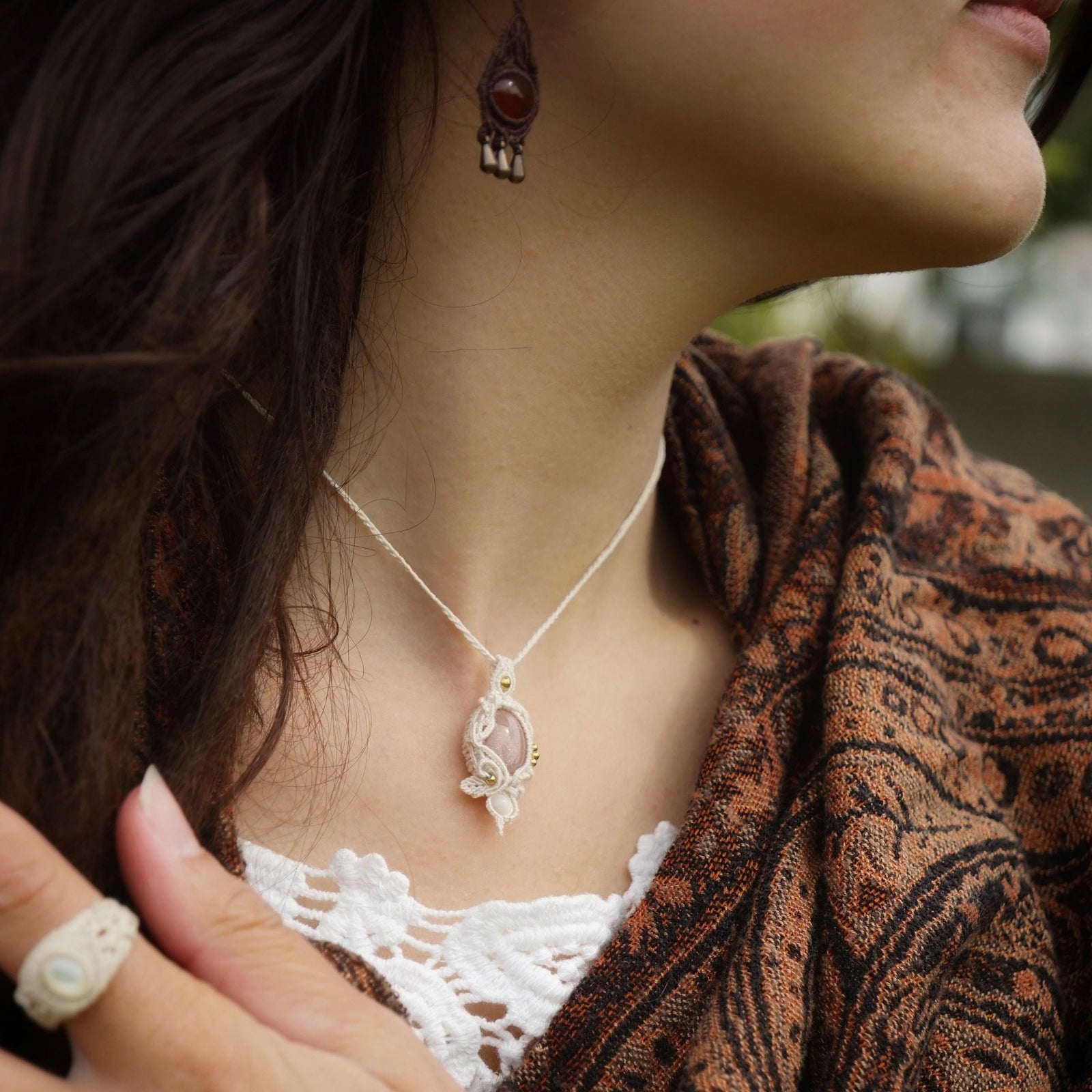 Collier pierre de soleil pêche en micro macramé artisanal, porté par une femme à la peau claire et cheveux bruns, vêtue d’une étole ethnique marron et orange.