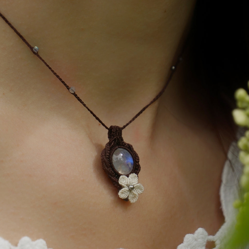 Collier elfique en labradorite blanche porté par un modèle à peau claire et cheveux bruns, vêtue d’habits féériques en dentelle blanche, bijou bohème artisanal réglable. Coton et Astrance