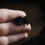 Boucles d’oreilles gothique florales noires tenues en main, bijou sombre elfique et élégant. Coton et Astrance