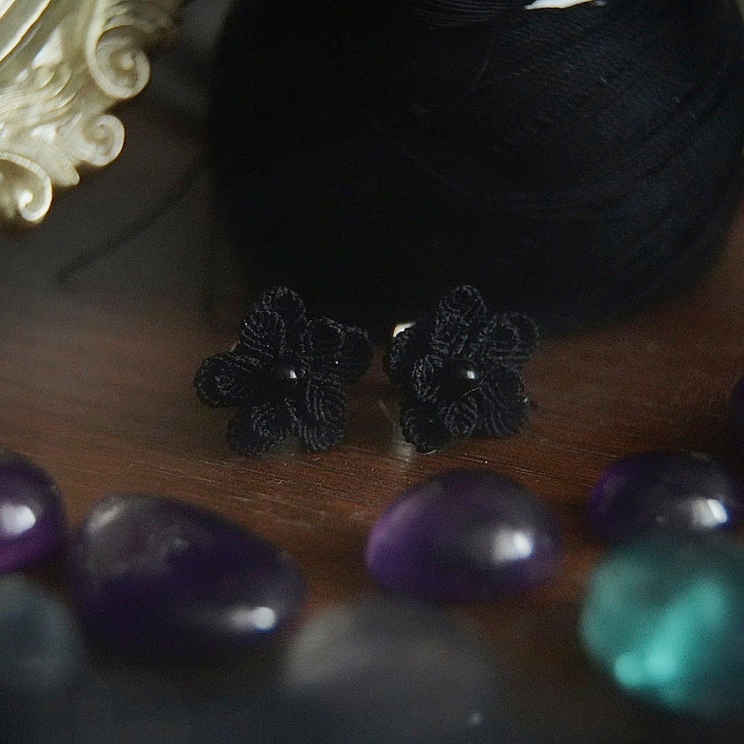 Bijou floral gothique en coton noir posé sur fond sombre, boucles d’oreilles artisanales fait main Coton et Astrance. 