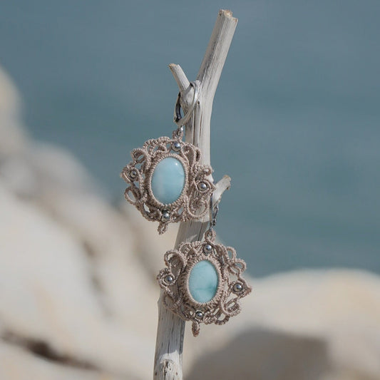 Boucles d'oreilles Trésors d'Ecume composée d'une Larimar bleu ciel ovales, mini Perles rondes en acier inoxydable argenté pour le côté luxe et précieux. Dormeuses en acier inoxydable pour un port assuré. Fil de Coton couleur lin naturel (beige gris) de 0, 5 mm tissé en micro-macramé en relief version celtique. Bijoux en vertical sur un bois flotté avec fond marin et plage, cailloux blanc et océan bleu. Ambiance sirène, plage et tropiques, bohème et hippie. Parfait pour les tenues mariage et festivals. 