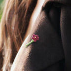 Broche florale rouge en micro macramé avec cœur doré, accessoire artisanal bohème et elfique, épinglée sur veste en laine marron foncé.
