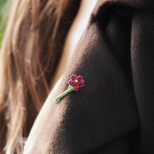 Broche florale rouge en micro macramé avec cœur doré, accessoire artisanal bohème et elfique, épinglée sur veste en laine marron foncé.