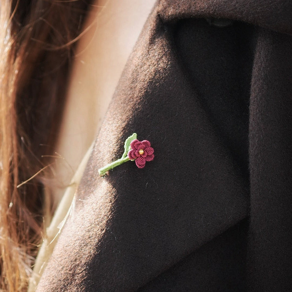 Broche florale rouge en micro macramé avec cœur doré, accessoire artisanal bohème et elfique, épinglée sur veste en laine marron foncé.