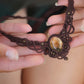 Collier large en micro macramé de couleur marron foncé, jaune ambré et bronze. Motif tissé en micro macramé avec ambiance entrelacs celtiques et arabesques elfiques. Présence d'une pierre centrale ovale de grande taille jaune translucide, gouttes bronze, forme V avec mini perles ronde bronze parsemées. Photo ambiance bohème hippie avec une touche d'élégance. Bijou posé à plat dans 2 mains en coupe à peau claire. jupe vert forêt en velours côtelé à l'arrière