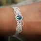Bracelet large asymétrique. Bijou dentelle ambiance bohème hippie. Bracelet tissé en micro macramé avec fil de coton écru de 0.5 mm avec une pierre ovale de chrysocolle couleur bleu turquoise et marron foncé chocolat. Présence de part et d'autre de façon symétrique des perles en acier inoxydable argentées. Système de réglage à coulisse tubulaire à l'arrière. Design en relief et en torsade entrelacées celtiques. Ambiance plages, festival d'été, tribal. Bijou porté fond bois clair