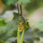 Collier elfique floral en citrine et macramé, fait main en France. Pièce artisanale réglable de la collection Clairière de Miel, photographiée au cœur de la nature parmi des feuilles de courge pour souligner son inspiration bohème et féérique.