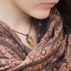 Collier elfique réglable en micro macramé avec citrine ovale jaune pâle et fleur orange dorée. Bijou floral et lumineux de la collection Clairière de Miel, porté par une femme à la peau claire et cheveux bruns.