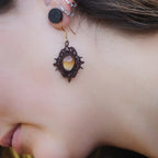 « Boucles d’oreilles elfiques losange en citrine dorée et grenat rouge, portées sur modèle à peau claire et cheveux bruns – Bijoux bohèmes artisanaux en micro macramé fait main en France »