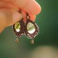 Boucles d'oreilles de style celtique elfique. Bijou féminin composé de : un tissage en relief avec arabesques en micro macramé avec du fil de coton marron foncé chocolat, pierre naturelle de citrine de forme goutte couleur jaune miel accompagné d'une perle ronde en citrine de 3 mm, d'un crochet doré en acier et d'une micro goutte bronze. Le bijou est présenté tenu dans une main avec une transparence évidente et un rayon de soleil qui traverse la pierre